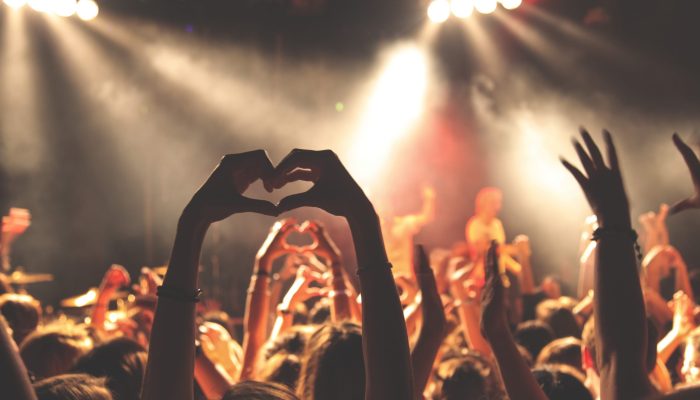 Publikum ved en koncert laver hjerte-tegn med hænderne.