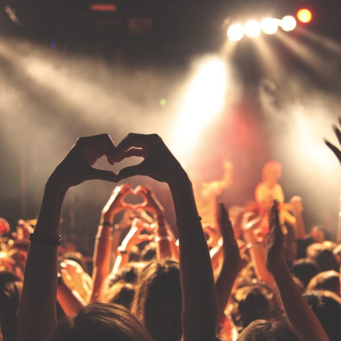 Publikum ved en koncert laver hjerte-tegn med hænderne.